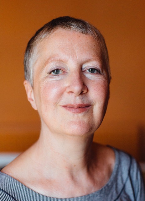 Woman with short dark hair against an orange background, looking straight to camera
