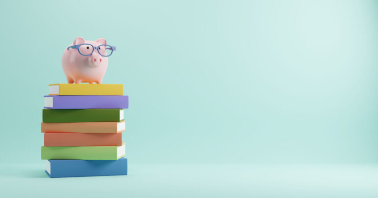 A piggy bank wearing glasses on top of a pile of books
