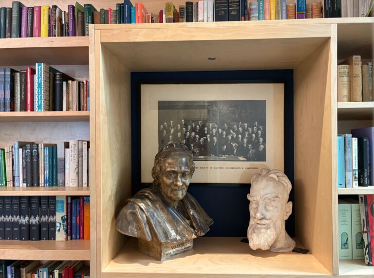 A bookshelf and busts with a black and white framed photo in the background