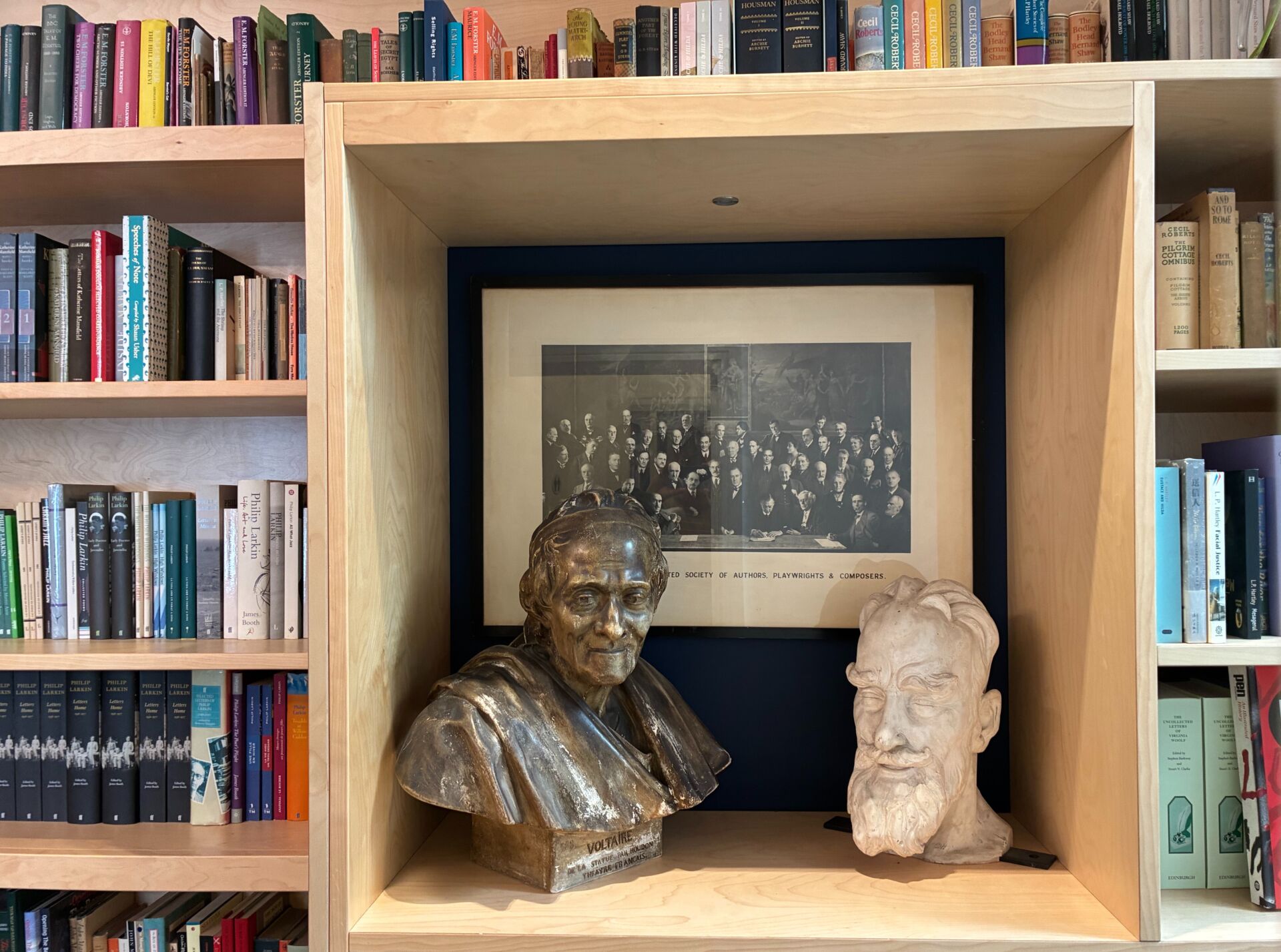 A bookshelf and busts with a black and white framed photo in the background