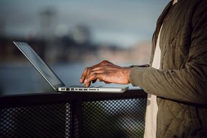 Side view of crop anonymous black male freelancer in casual wear using laptop to work on remote project while standing on open terrace