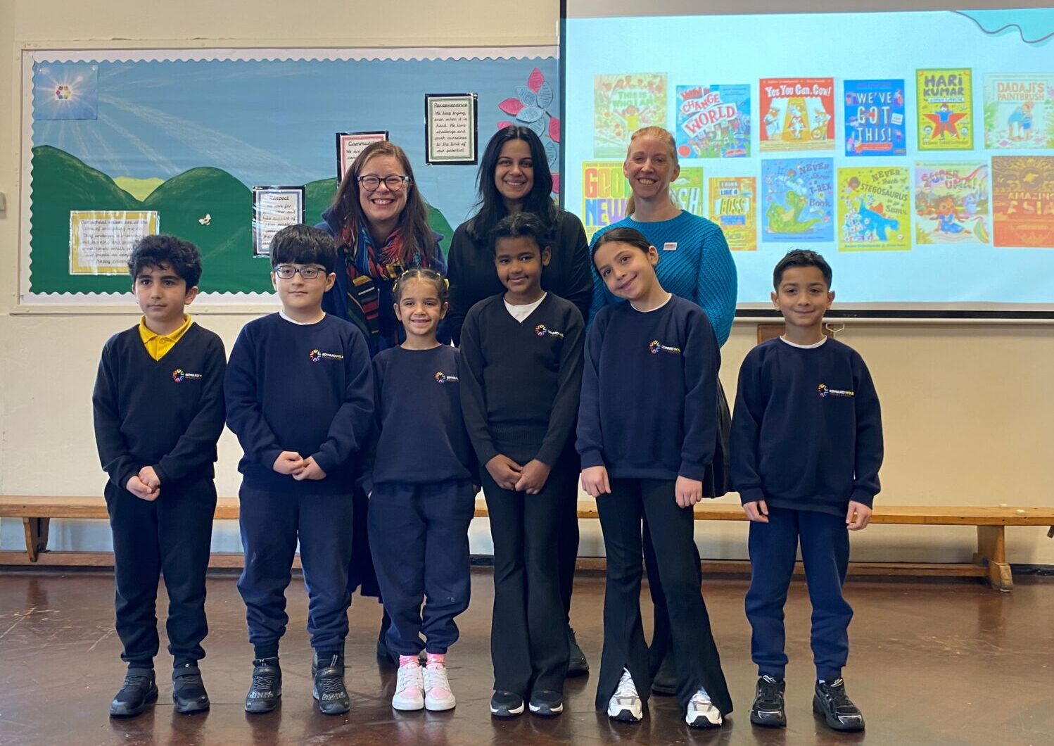 A group of adults and primary school children standing in front of a presentation celebrating books.
