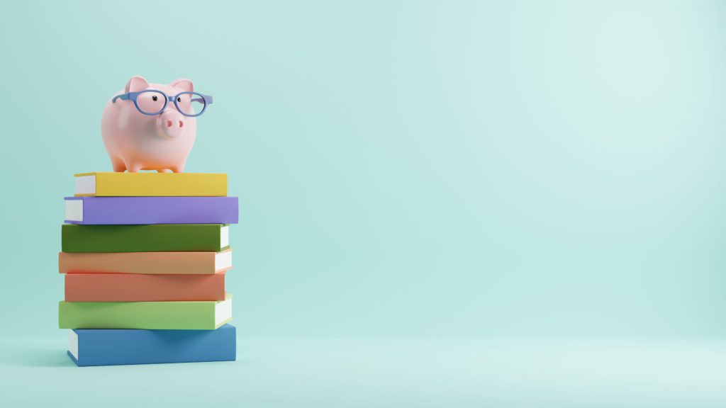 A piggy bank wearing glasses on top of a pile of books