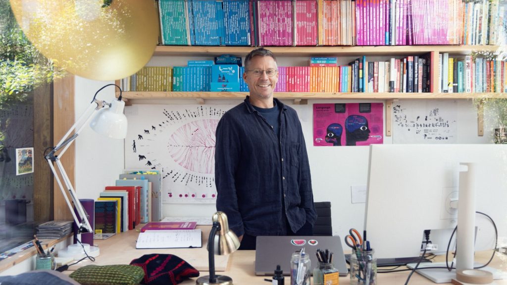 Chris Haughton standing in his studio with a bookshelf behind him and desk in front of him