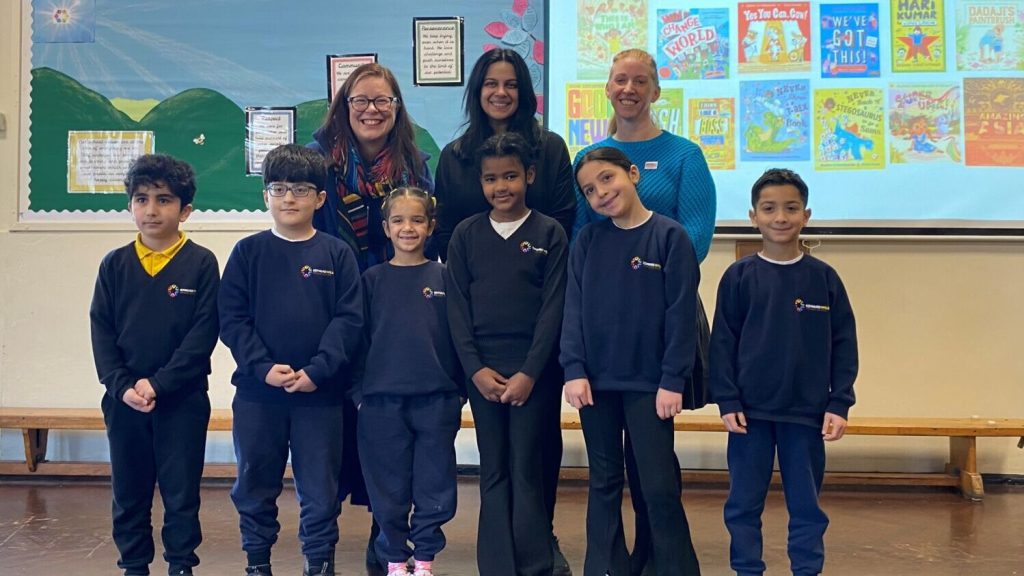 A group of adults and primary school children standing in front of a presentation celebrating books.