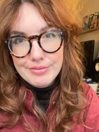 image shows white female with long brown hair and glasses wearing a red shirt.
